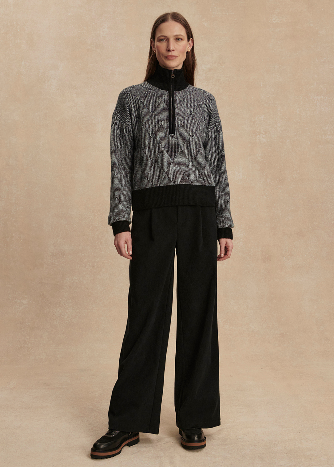 Woman wearing a black knit top with black pants against a tan background