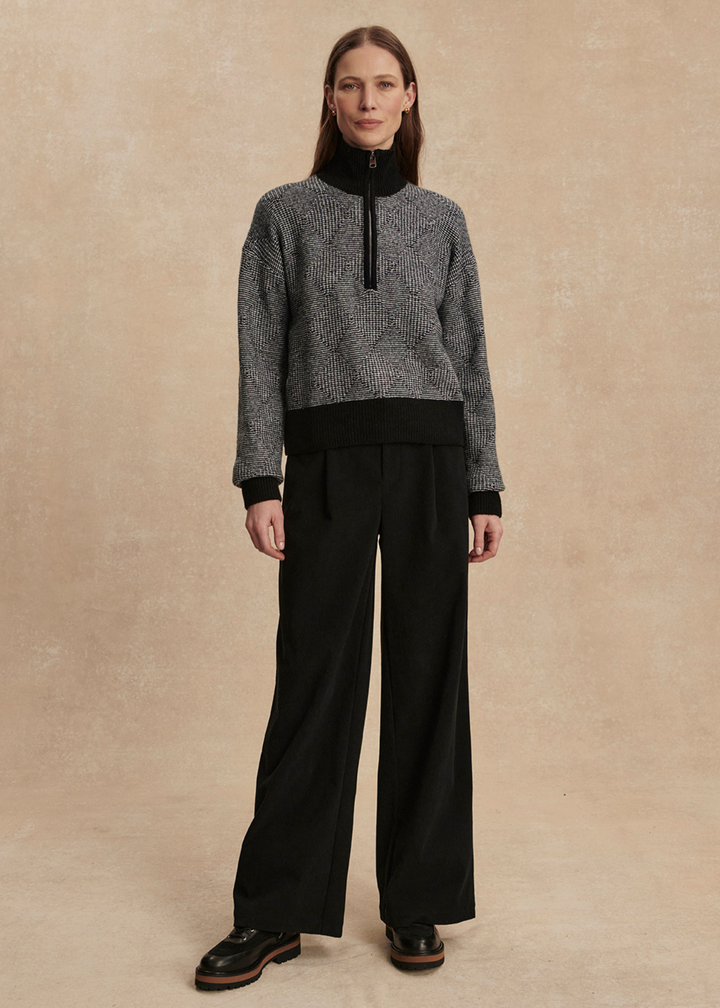 Woman wearing a black knit top with black pants against a tan background