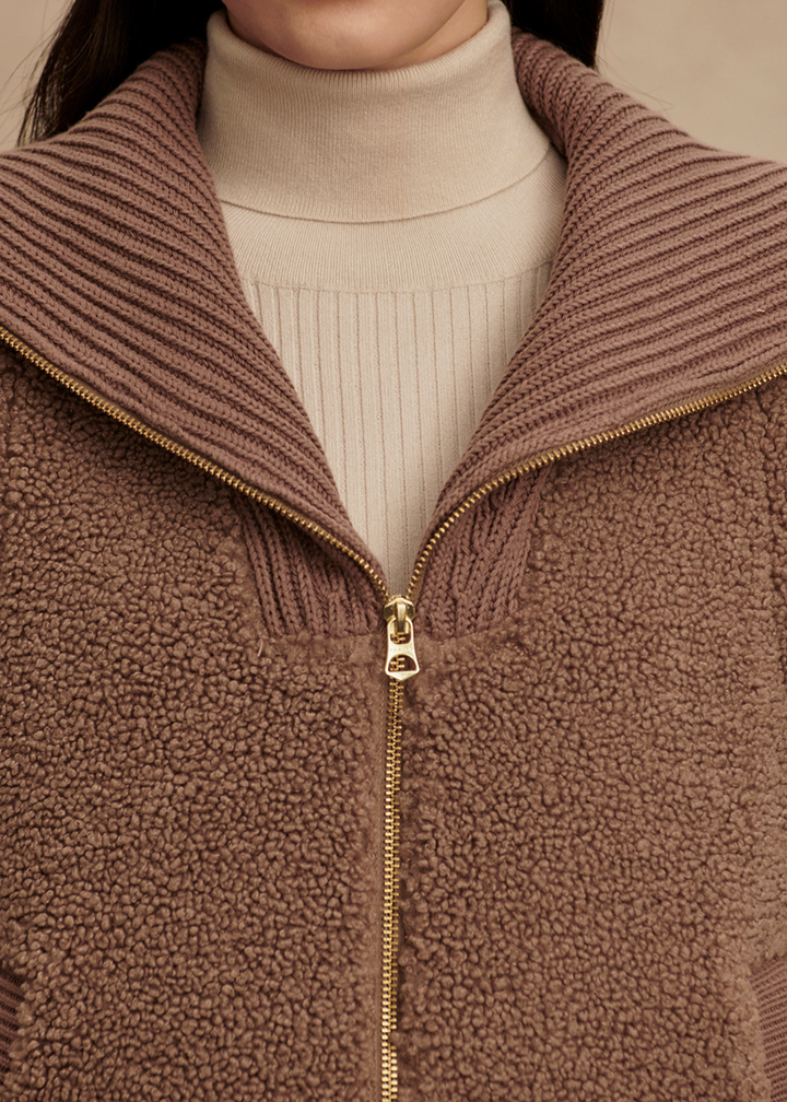 Close up of a brown vest with a gold zipper over a cream turtleneck