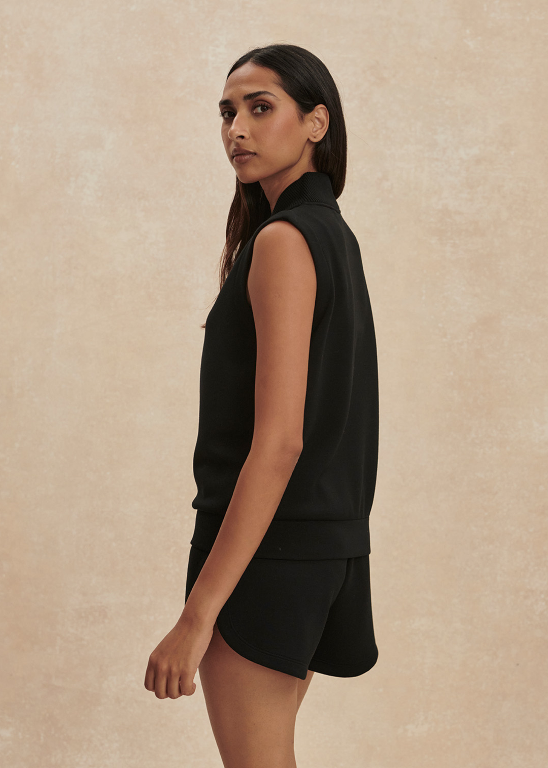 Woman turned to the side wearing a black half zip sleeveless top with matching shorts