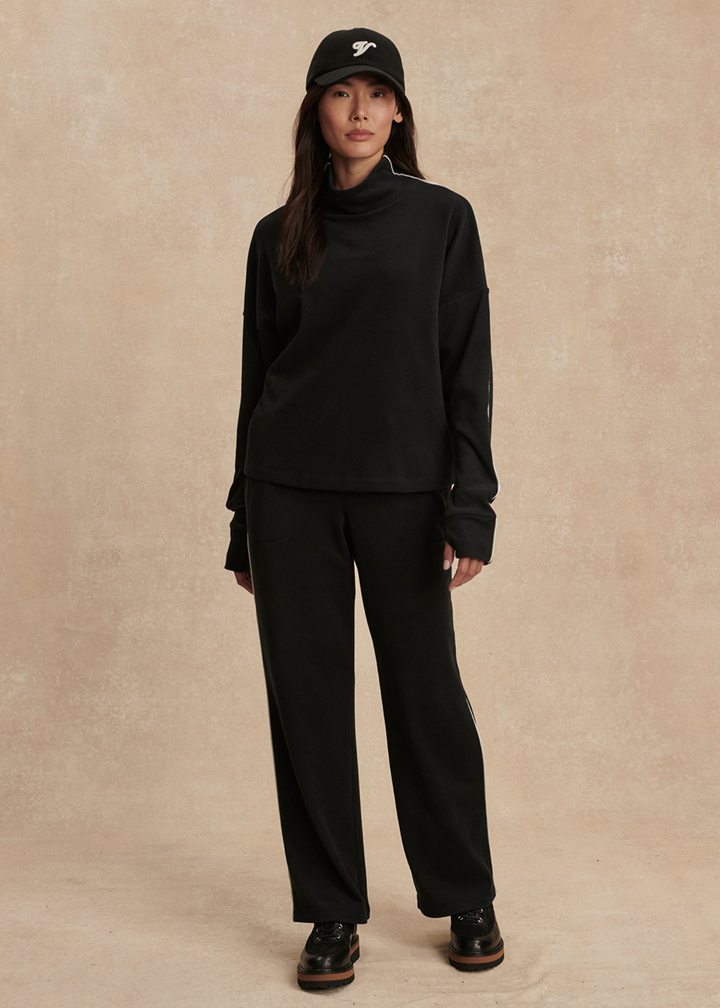 Woman wearing a black top and black pants against a tan background