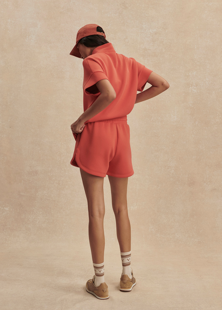 Woman wearing orange shorts with a half zip top