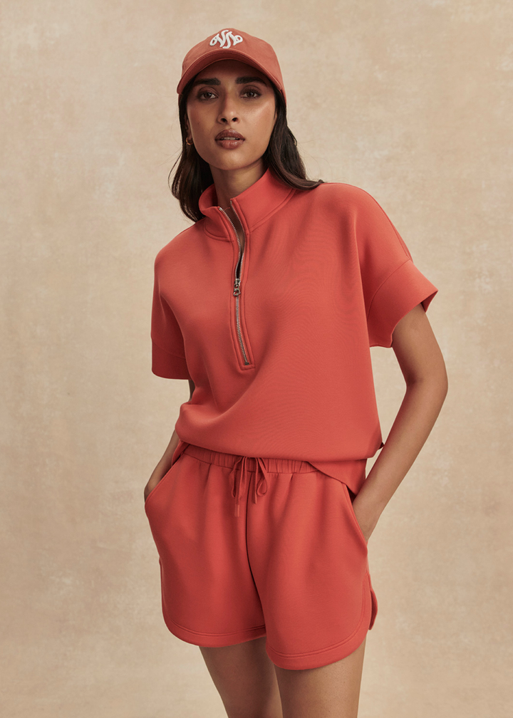 Woman wearing orange shorts with a half zip top