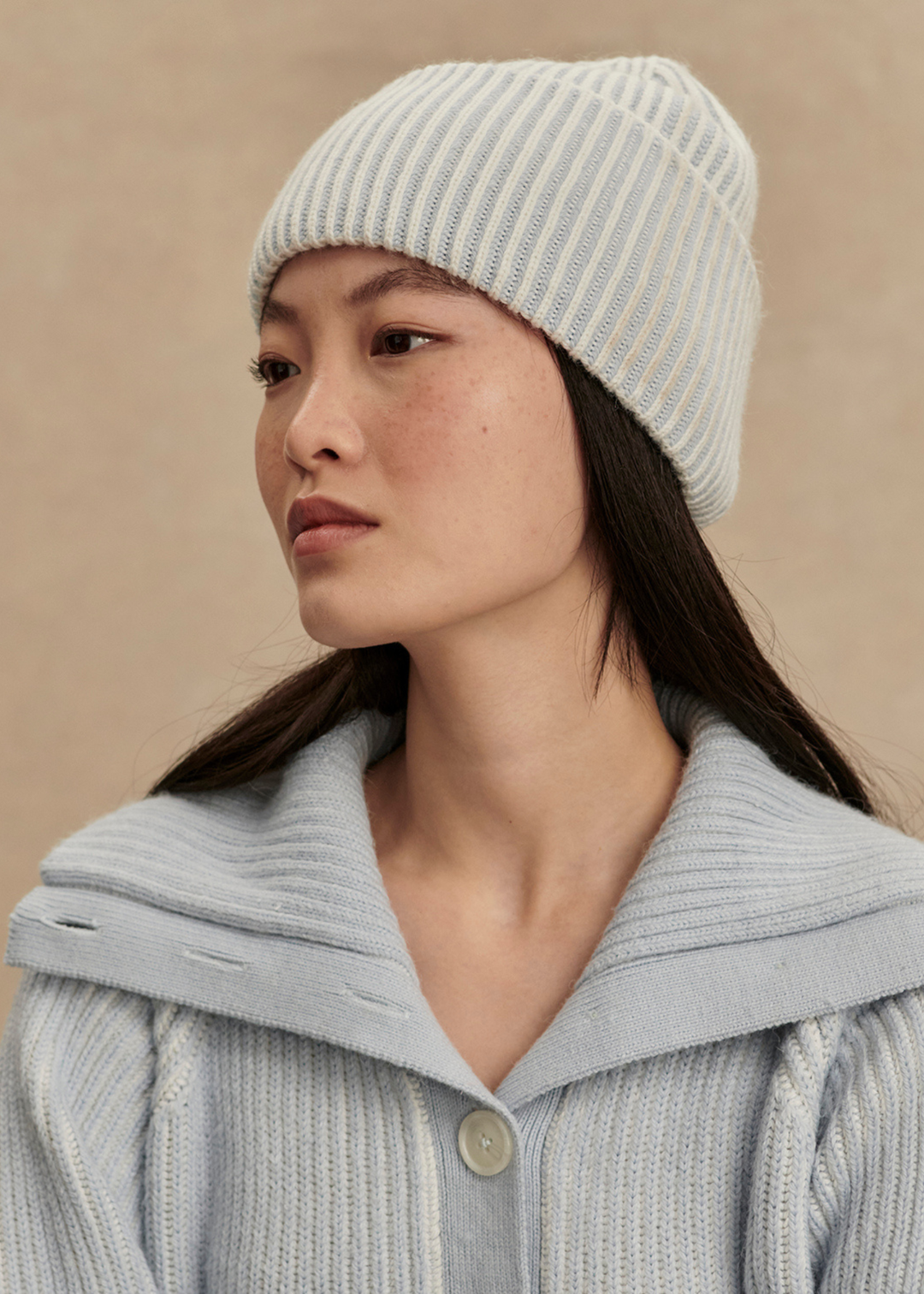 Woman wearing a light blue beanie and a light blue sweater in front of a tan background