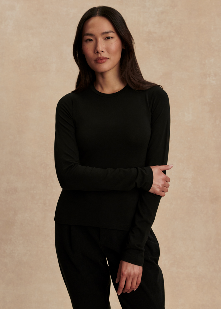 Woman wearing a black long sleeve tee with black pants in front of a tan background