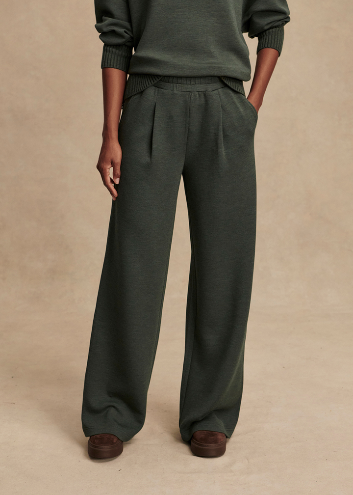 Close up of woman wearing dark green wide leg pants in front of a tan background