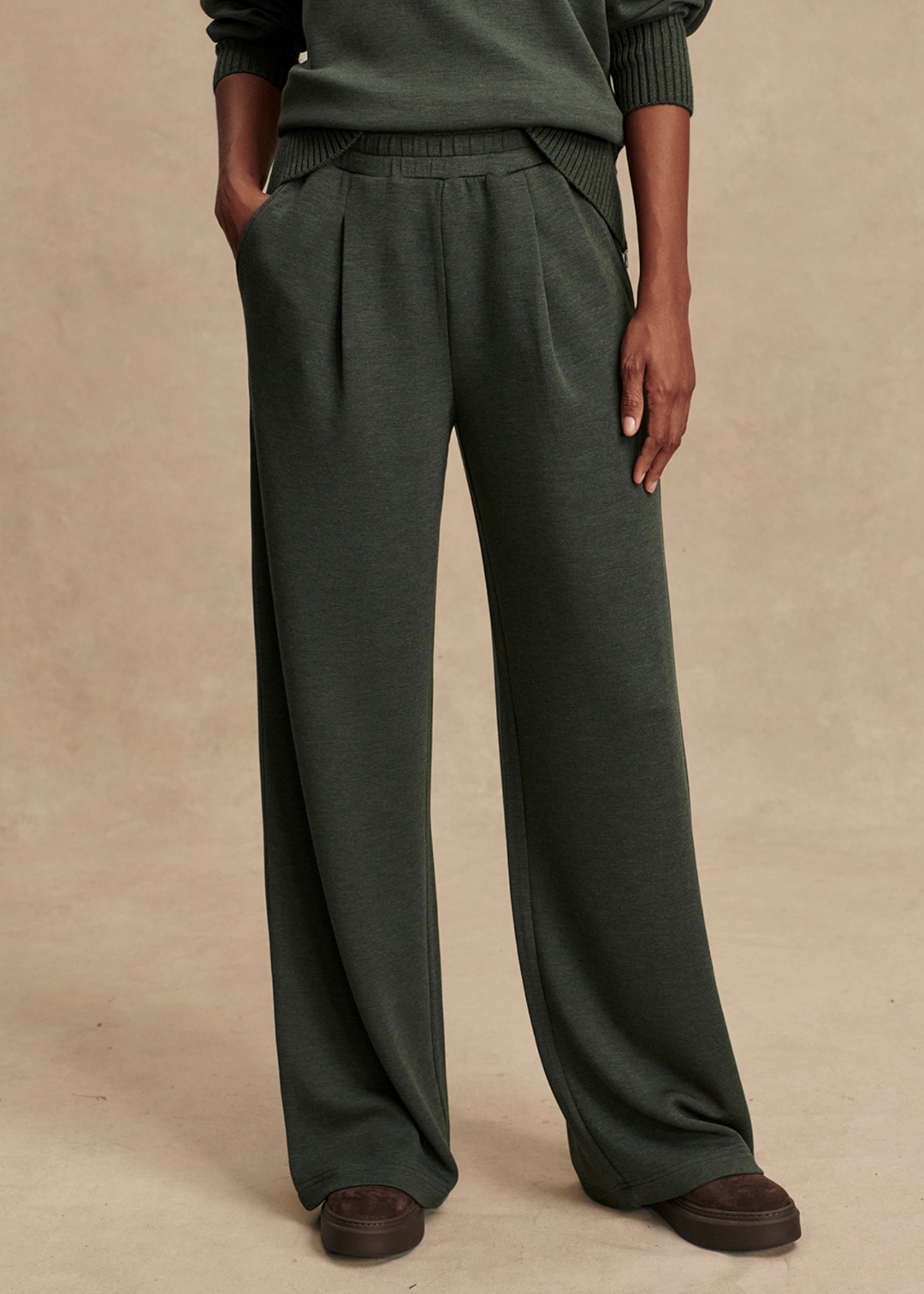 Close up of woman wearing dark green wide leg pants in front of a tan background