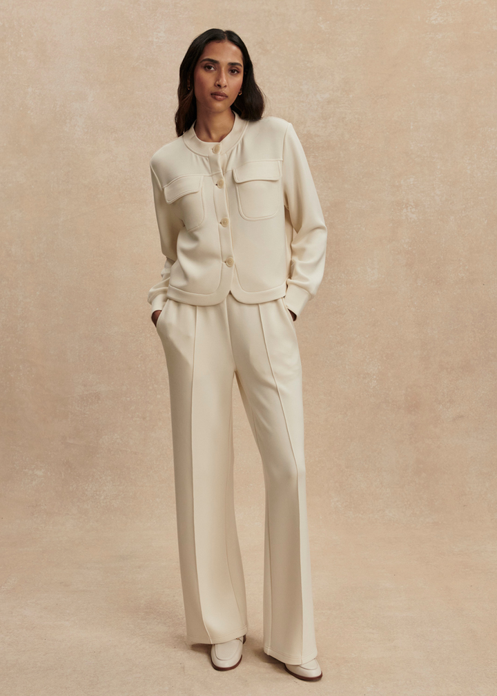 Woman wearing a cream button down sweater with matching pants against a tan background