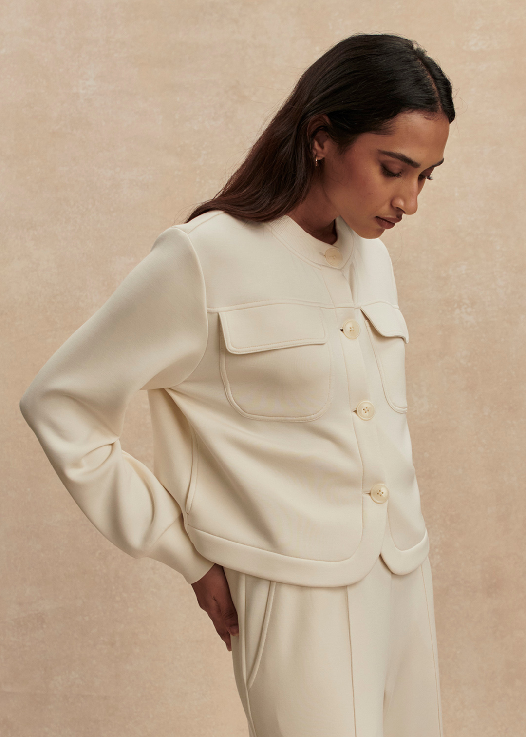 Woman wearing a cream button down sweater with matching pants against a tan background