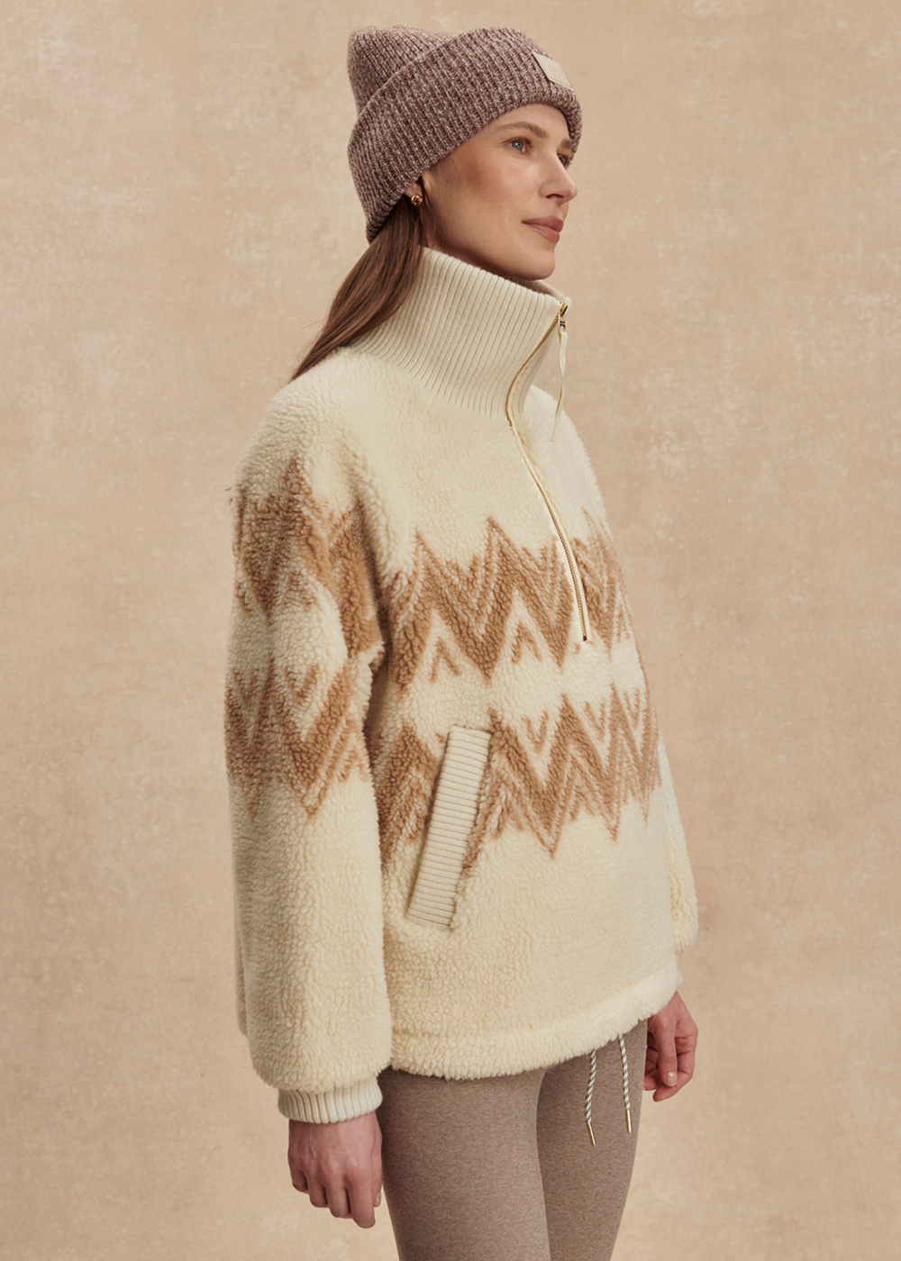 Woman turned to the side wearing a cream and brown half zip sherpa with a brown beanie and leggings