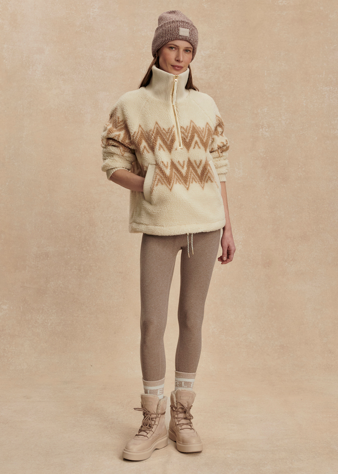 Woman wearing a cream and brown half zip sherpa with a brown beanie and leggings