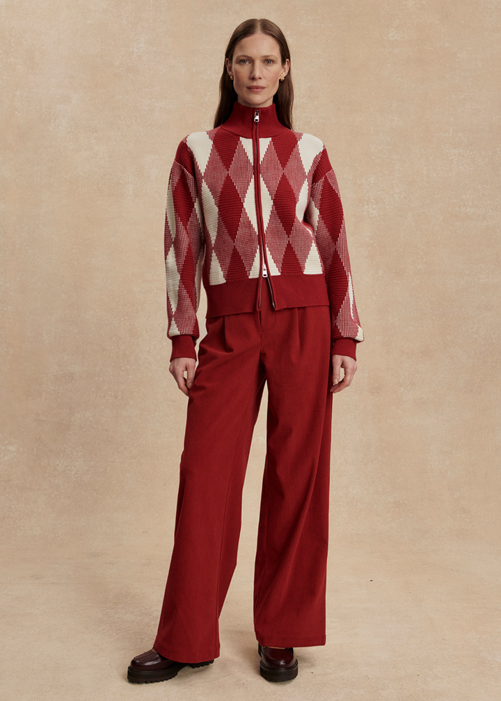 Woman wearing a red and white patterned sweater with red pants against a tan background