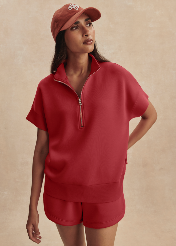 Woman wearing a pink/red short sleeve 1/2 zip sweatshirt with matching shorts