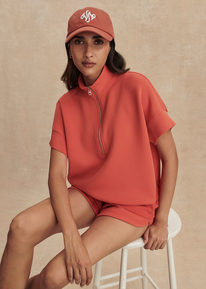 Woman wearing an orange half zip top with matching shorts