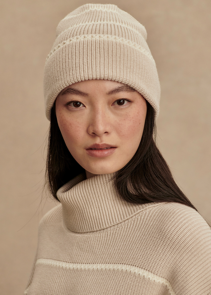 Woman wearing a tan and white striped beanie with a matching sweater in front of a tan background
