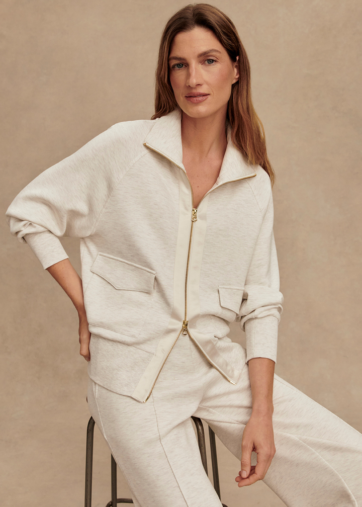Woman wearing an ivory zip up sweatshirt with matching pants in front of a tan background