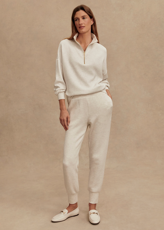 Woman wearing slim fit ivory sweatpants with a matching sweatshirt in front of a tan background