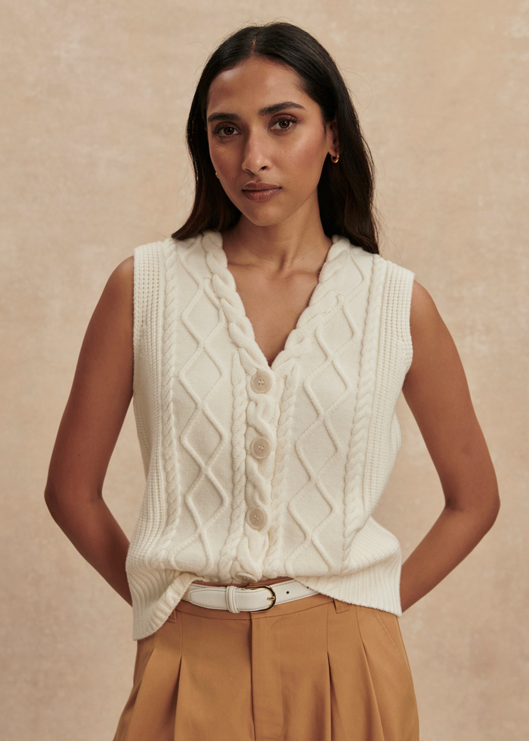 Woman wearing a cream cable knit sweater vest with brown pants
