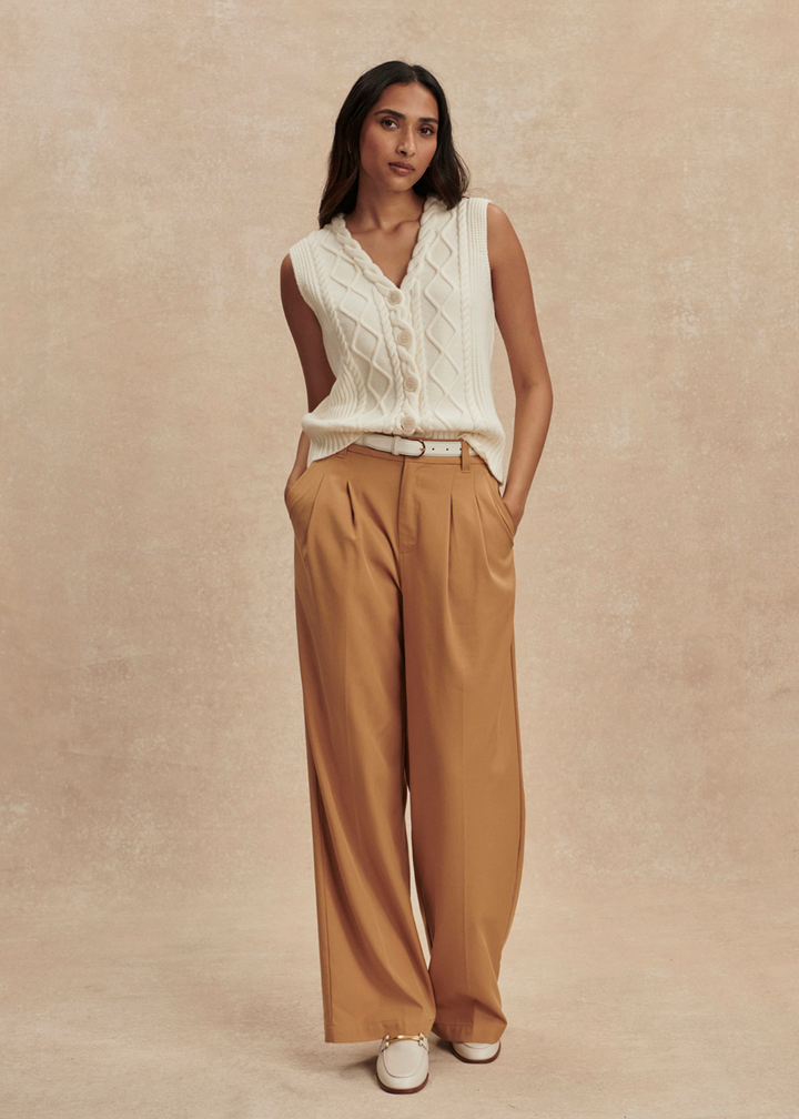 Woman wearing a cream cable knit sweater vest with brown pants