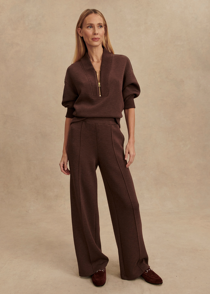 Woman wearing brown wide leg pants with a matching half zip sweatshirt in front of a tan background