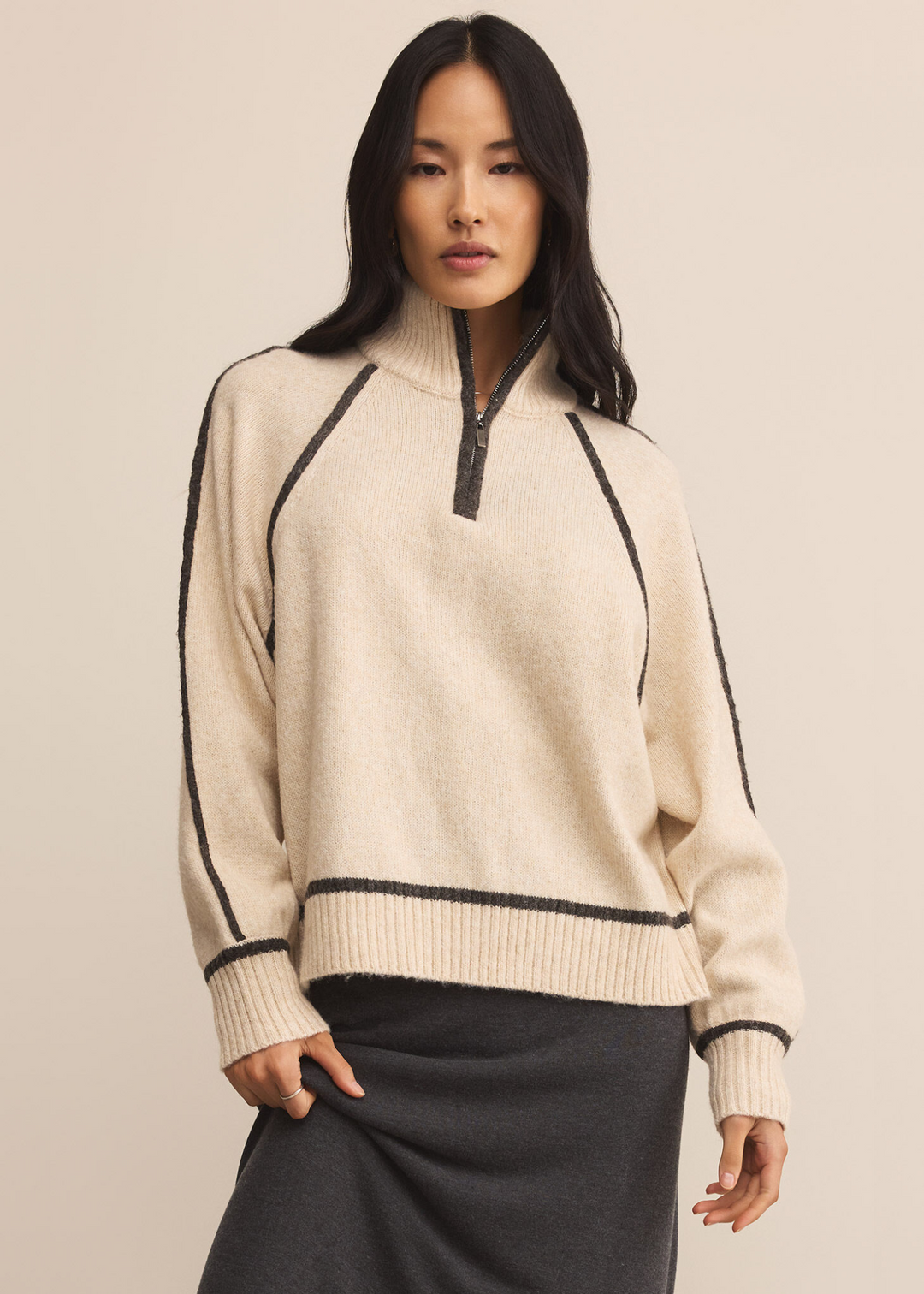 Woman wearing a cream colored half zip sweater with charcoal grey stripes and a turtleneck
