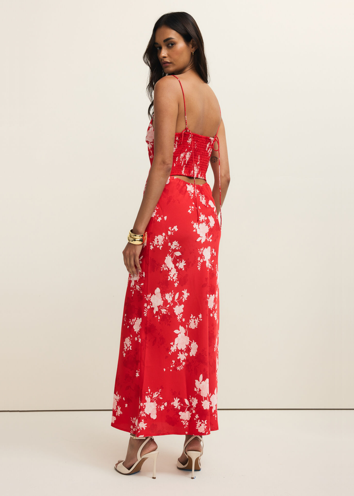Woman looking over shoulder wearing a red and white floral maxi dress against a white background