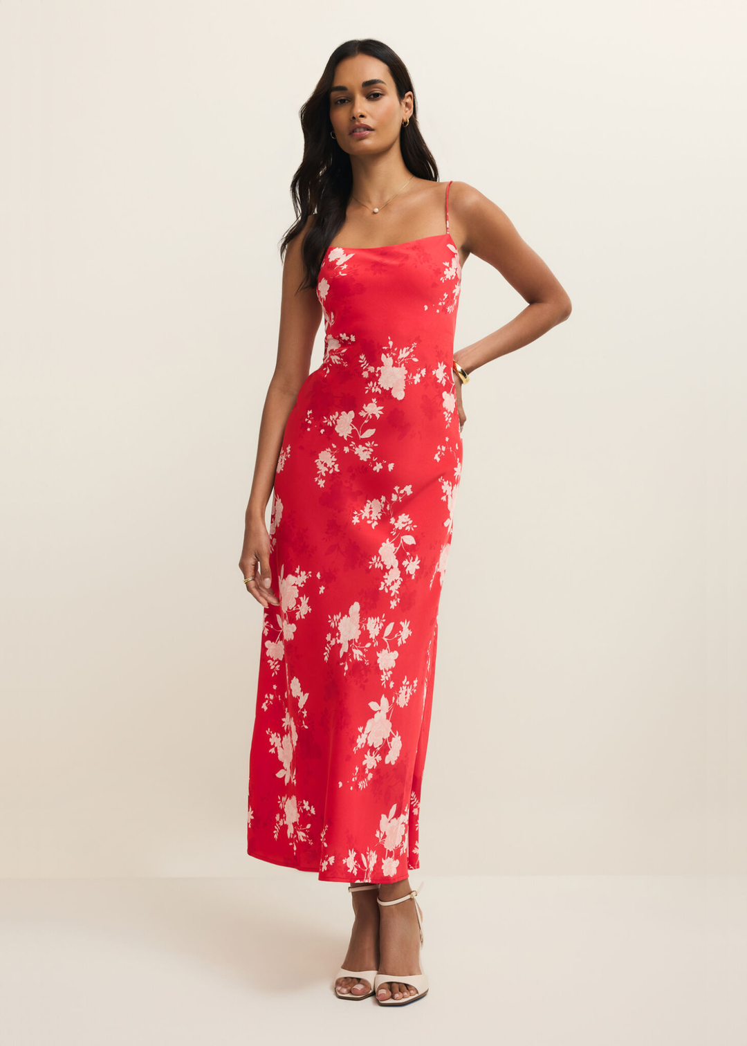 Woman with hand on hip wearing a red and white floral maxi dress against a white background