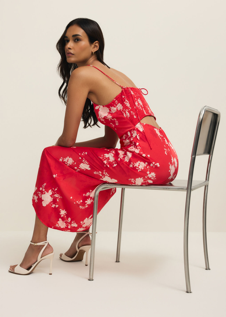 Woman sitting wearing a red and white floral maxi dress against a white background
