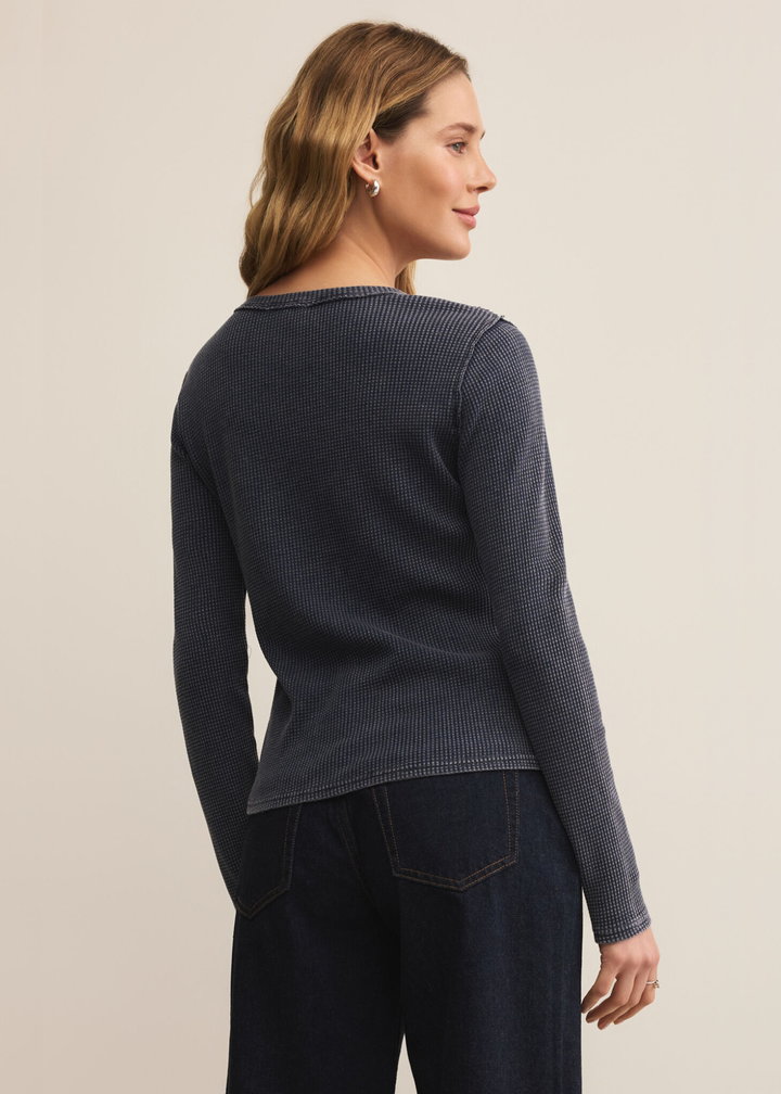 Woman turned around wearing a dark blue long sleeve tee with dark wash jeans against a white background