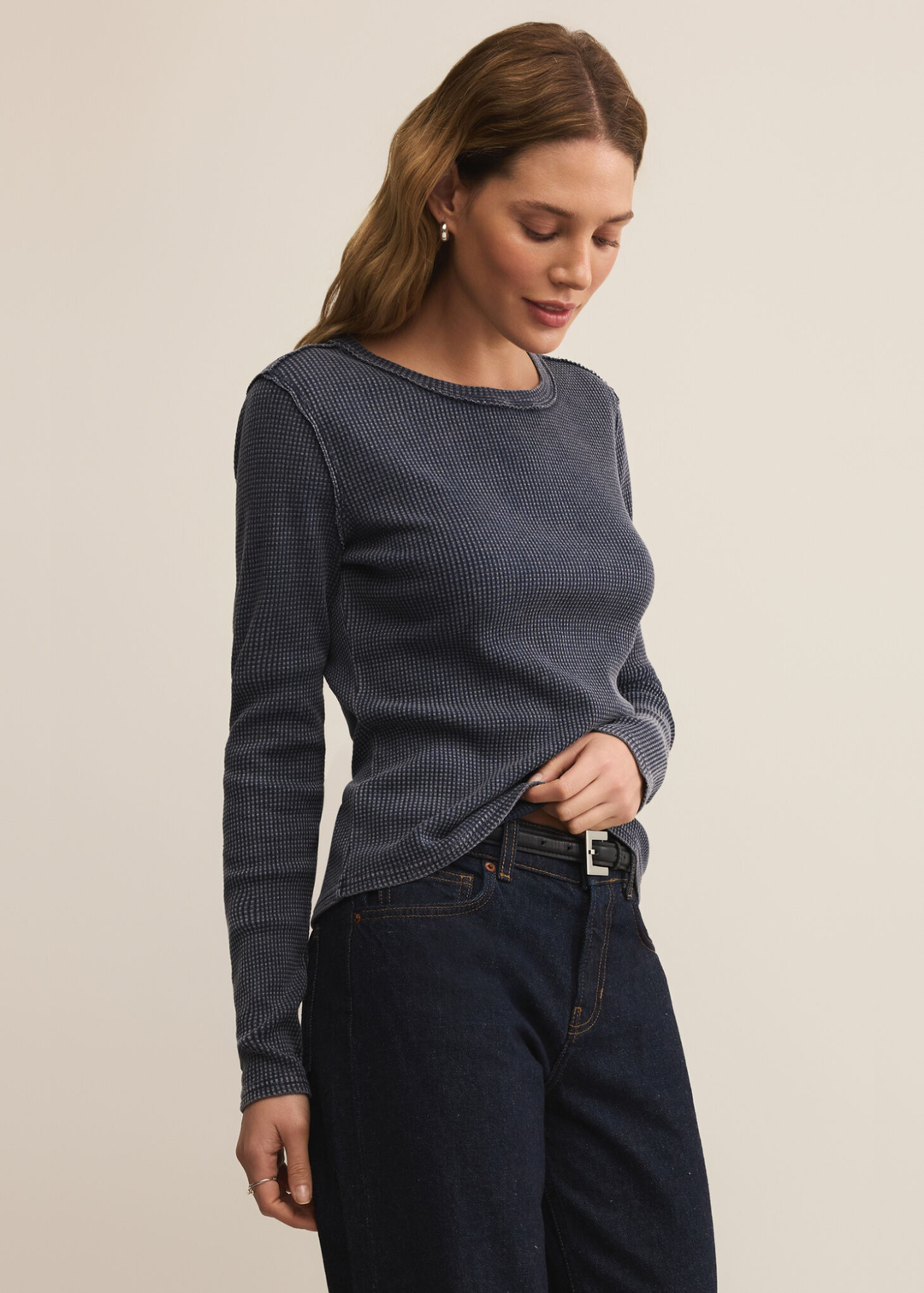 Woman wearing a dark blue long sleeve tee with dark wash jeans against a white background