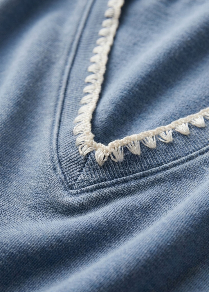 Close up of a blue knit denim sweatshirt with whipstitch trim