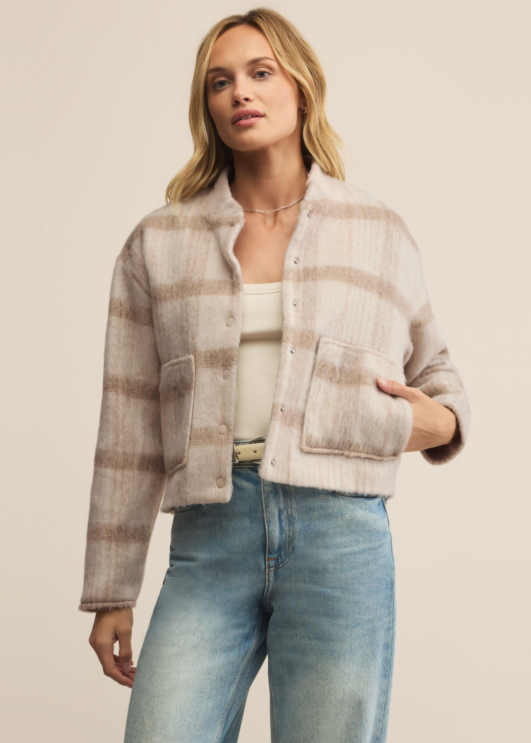 Woman wearing a tan and light brown plaid jacket with large front pockets and jeans