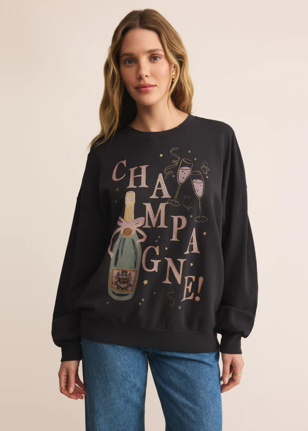 Woman wearing a grey sweatshirt with a champagne graphic and jeans