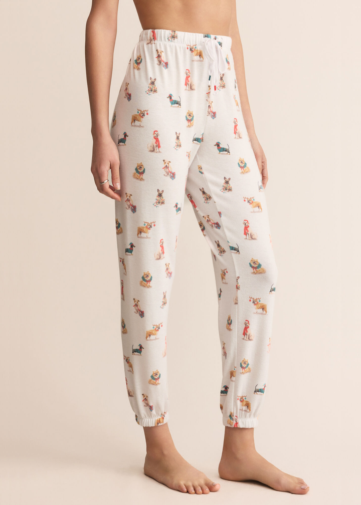 Woman turned to the side wearing white joggers with a dog graphic pattern in front of a tan background