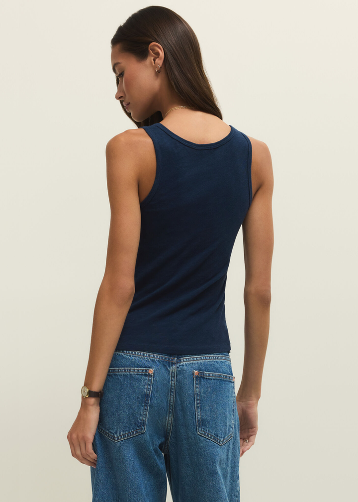 Woman turned around wearing a navy tank top with jeans against a white background