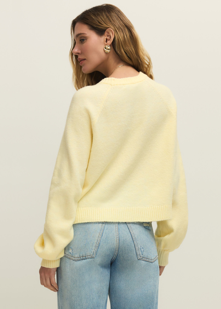 Woman turned around wearing a light yellow sweater with jeans against a white background