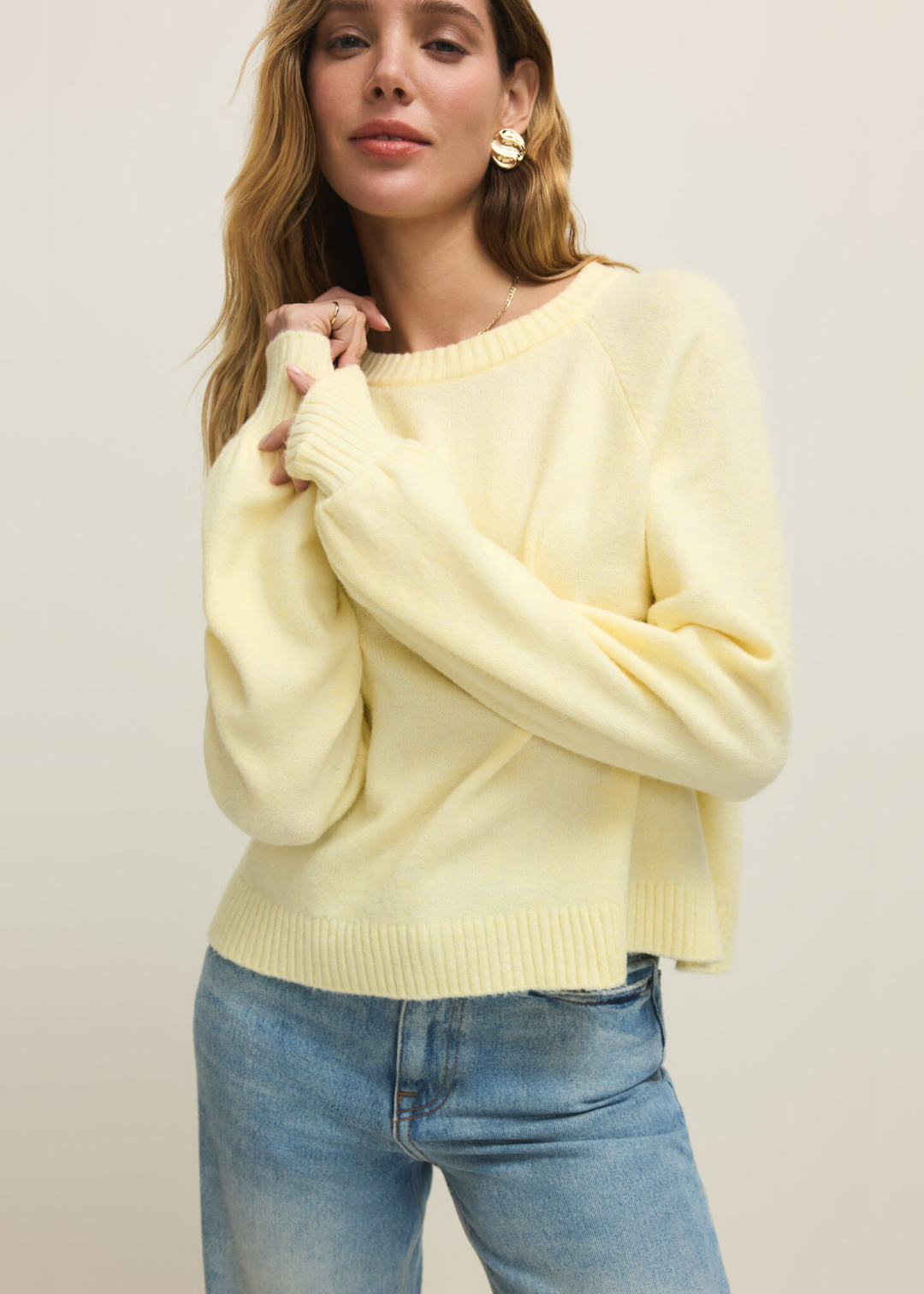 Woman wearing a light yellow sweater with jeans against a white background