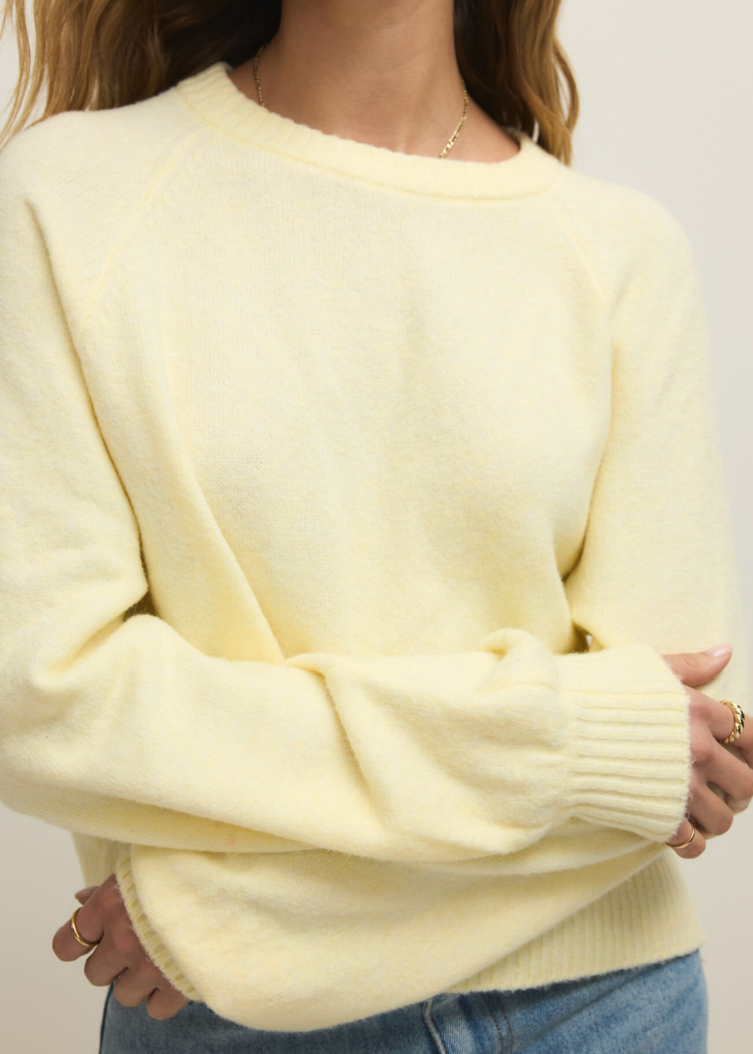 Close up of a woman wearing a light yellow sweater with jeans against a white background