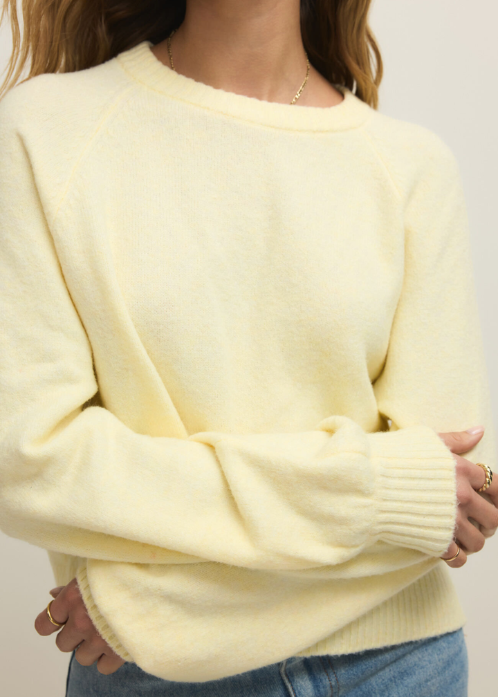 Close up of a woman wearing a light yellow sweater with jeans against a white background