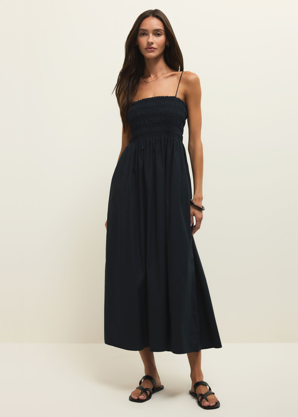 Woman wearing a black spaghetti strap midi dress against a white background