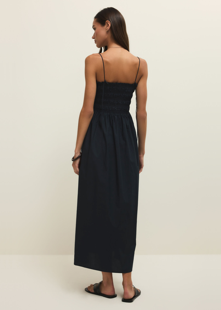 Woman turned around wearing a black spaghetti strap midi dress against a white background