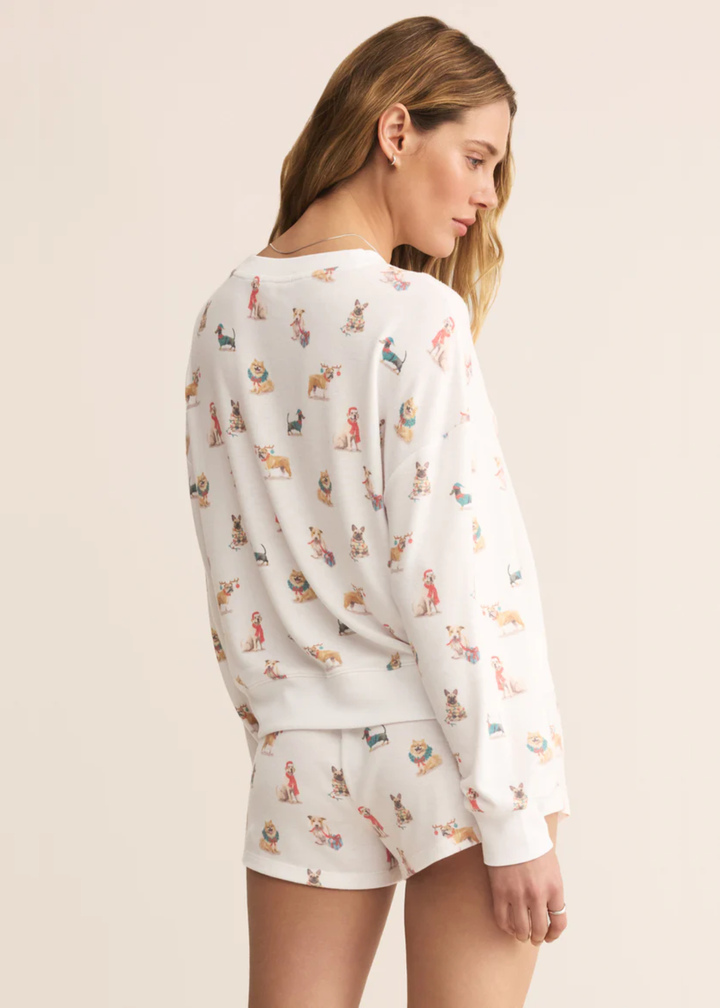 Woman turned around wearing a white long sleeve shirt with a Christmas dog pattern and matching shorts in front of a tan background