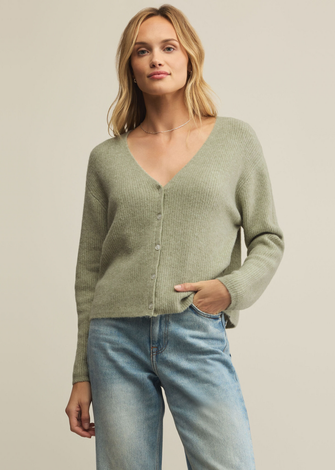 Woman wearing a green cardigan and jeans in front of a grey background