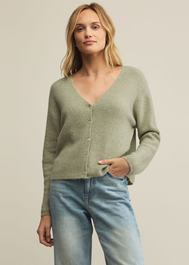 Woman wearing a green cardigan and jeans in front of a grey background