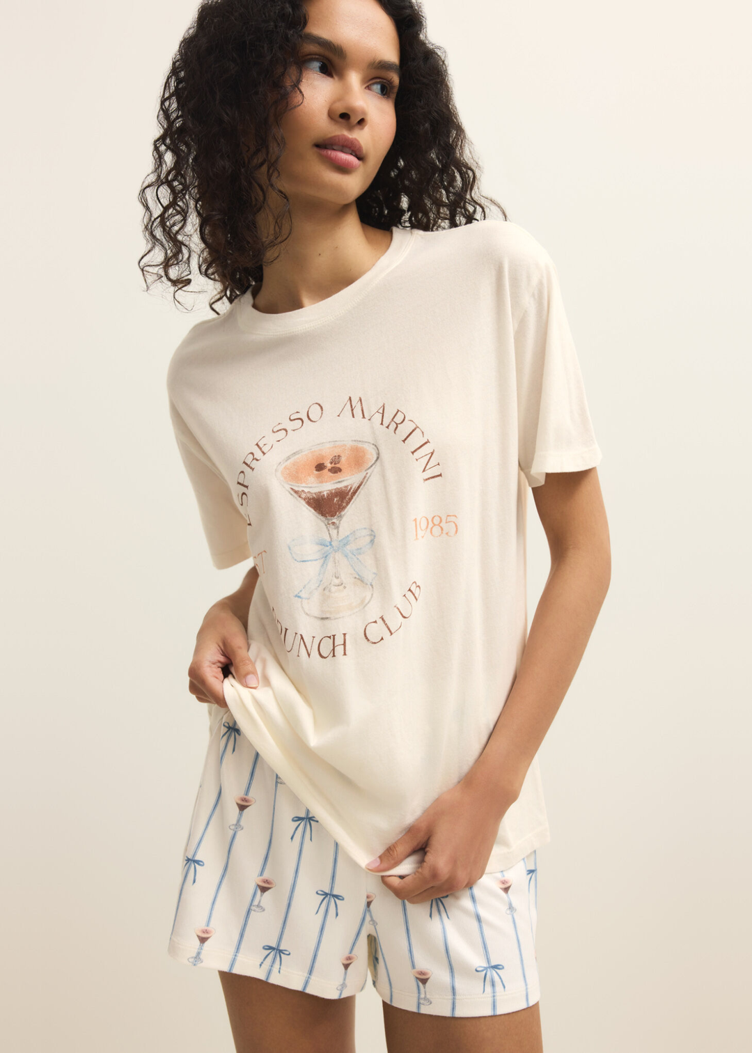 Woman wearing a white shirt with an espresso martini graphic and shorts against a white background