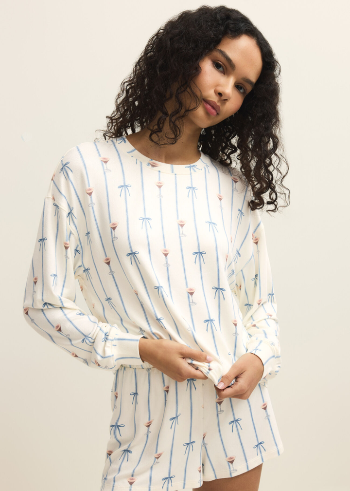 Woman wearing white shorts with a blue ribbon and espresso martini pattern and a matching long sleeve top