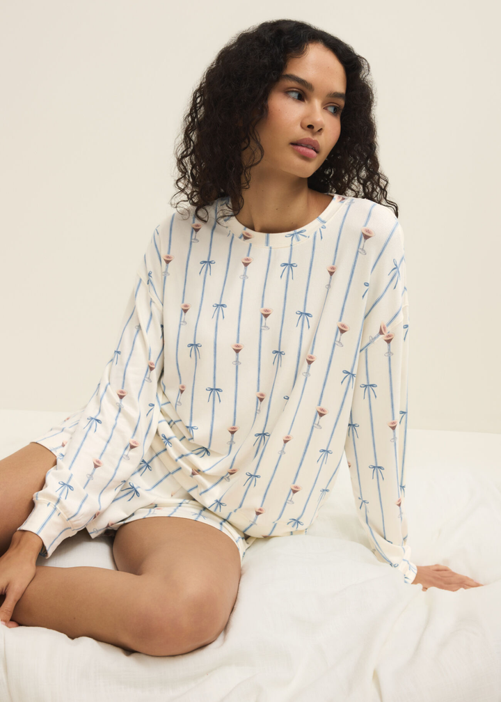 Woman wearing white shorts with a blue ribbon and espresso martini pattern and a matching long sleeve shirt