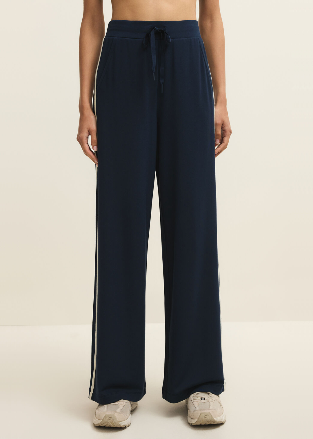 Woman wearing navy sweatpants with white side stripes against a white background