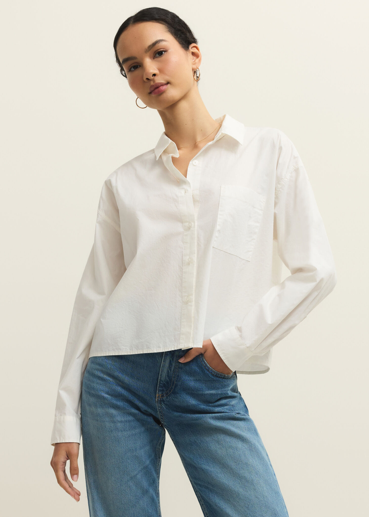 Woman wearing a white button down top with jeans and hand in pocket