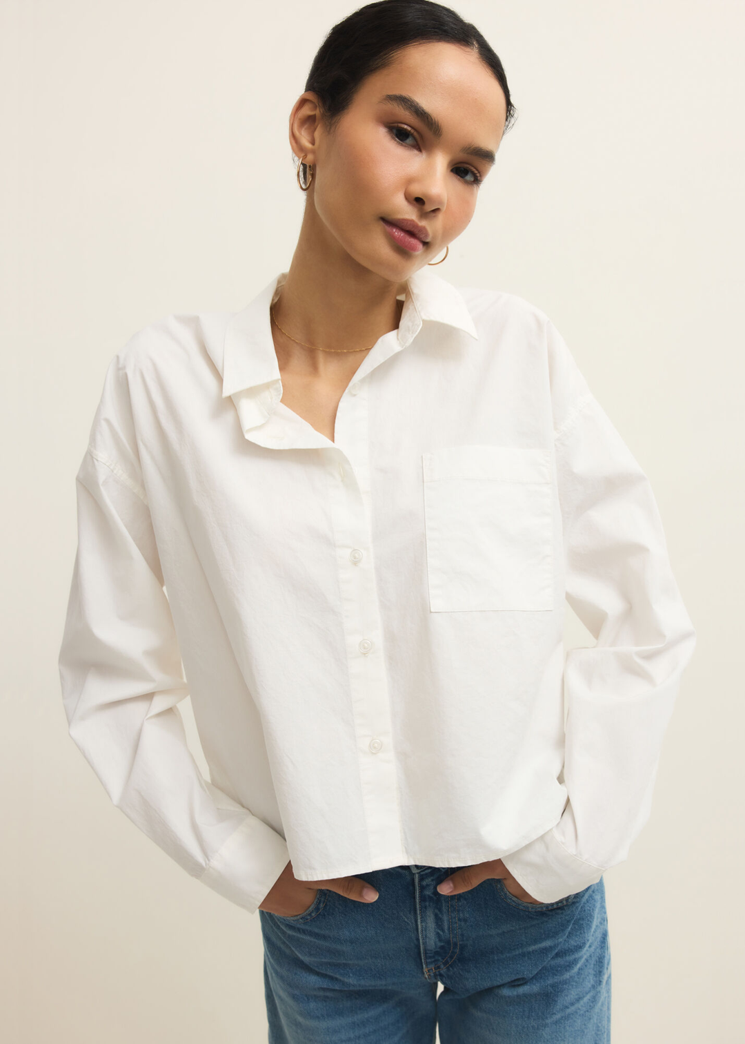 Woman wearing a white button down top with jeans with hands in pocket